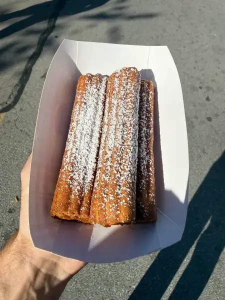 A hand holding a paper tray of three apple churros under powdered sugar
