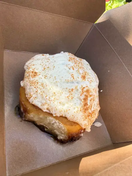 An apple cinnamon roll under thick white icing dusted with cinnamon, in a kraft paper box